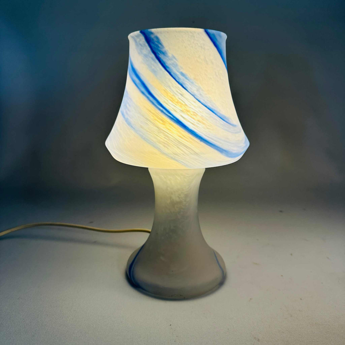 Einzelne Pilz-Tischleuchte eingeschaltet, überwiegend weißer Fuß mit zartem blauem Swirl