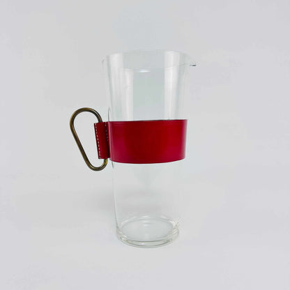Ansicht der schlanken transparenten Glaskaraffe mit roter Lederfassung und Messinggriff der 1950er