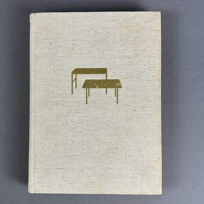 Draufsicht auf den beigefarbenen Leineneinband von Das Möbelbuch mit goldgeprägtem Tischsymbol von 1958