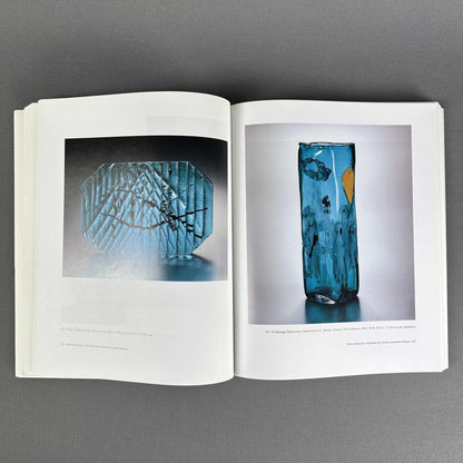 Offene Buchseiten mit blauer Strukturglasschale und hoher türkisfarbener Vase mit gelbem Dekor