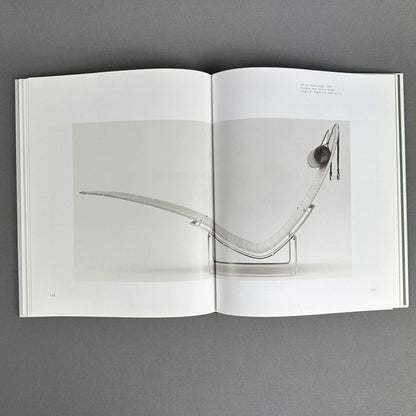 Buchseiten mit einer geschwungenen Liege auf Stahlgestell in einer großformatigen Schwarzweißfotografie