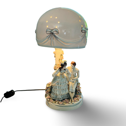 Eingeschaltete Tischlampe mit warm leuchtendem Schirm über dem figürlichen Porzellansockel