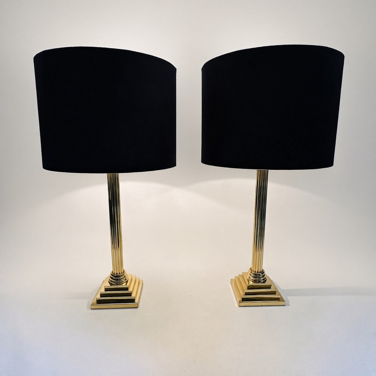 Paire de lampes colonnes Hollywood Regency en laiton allumées, lumière chaude sur les socles à gradins