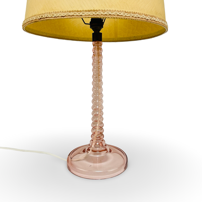 Gesamtansicht der Tischlampe mit rosa Glasschaft, cremegelbem Schirm und schwarzer Bajonettfassung