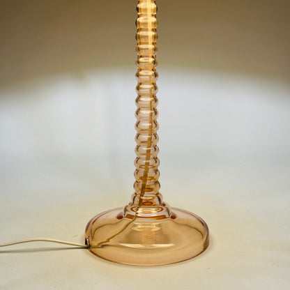 Leuchtender Ausschnitt des rosa Glasschafts und transparenten Rundfußes der Tischlampe