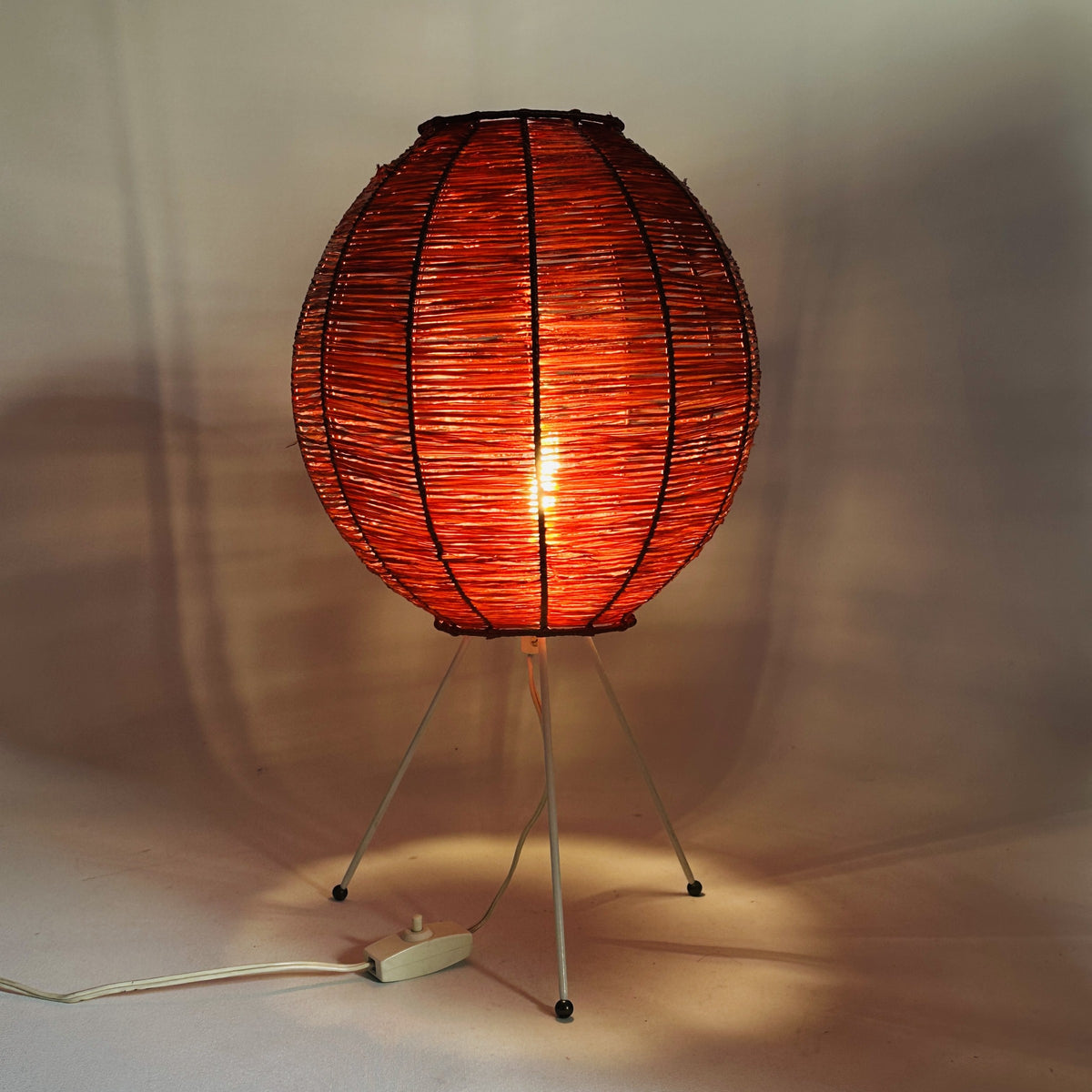Eingeschaltete Bast-Tischleuchte, warmes rotes Licht scheint durch das Geflecht, 1950er