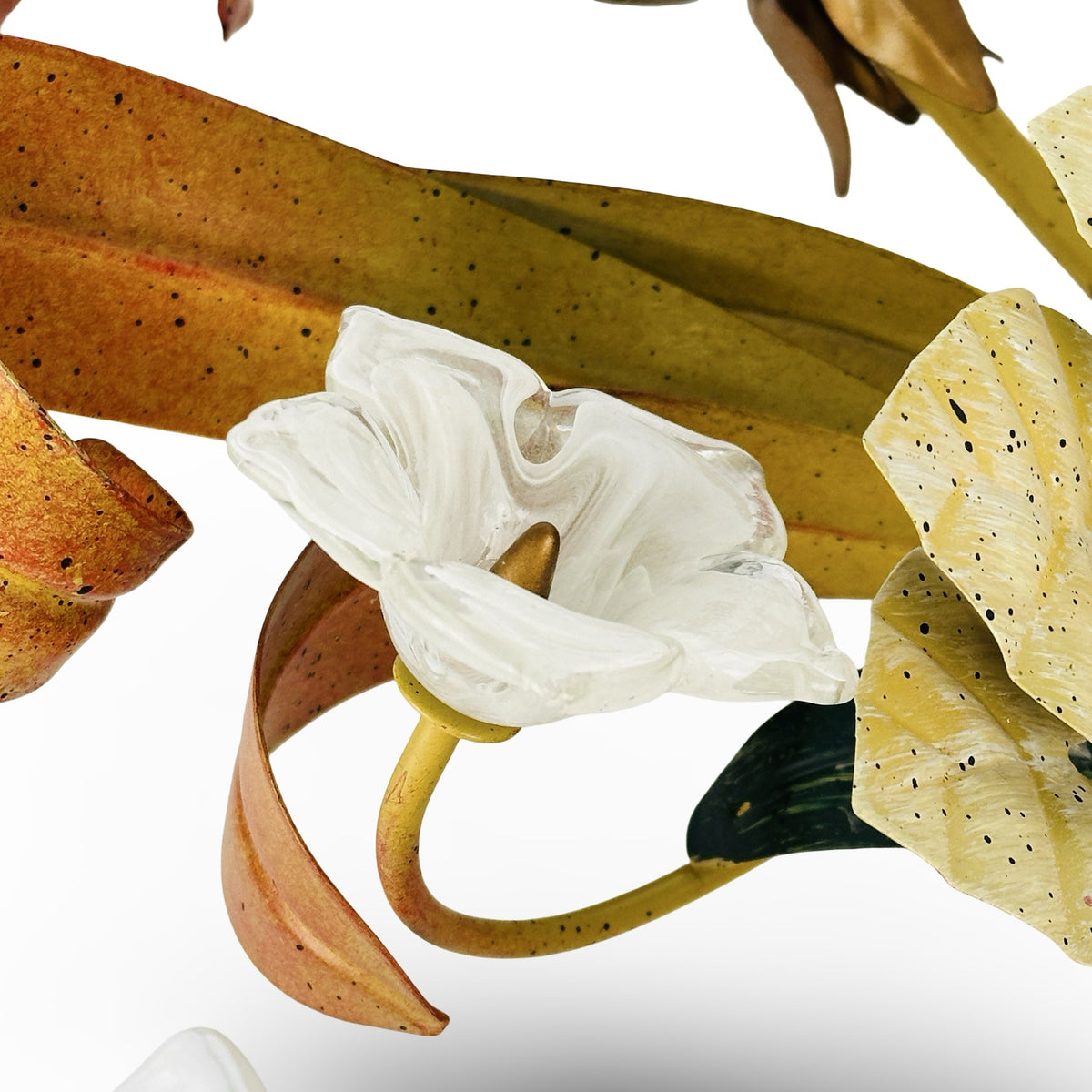 Nahaufnahme einer kleinen Glasblüte aus klarem Glas mit weißen Schlieren und messingfarbenem Stempel vor gesprenkeltem Blattband