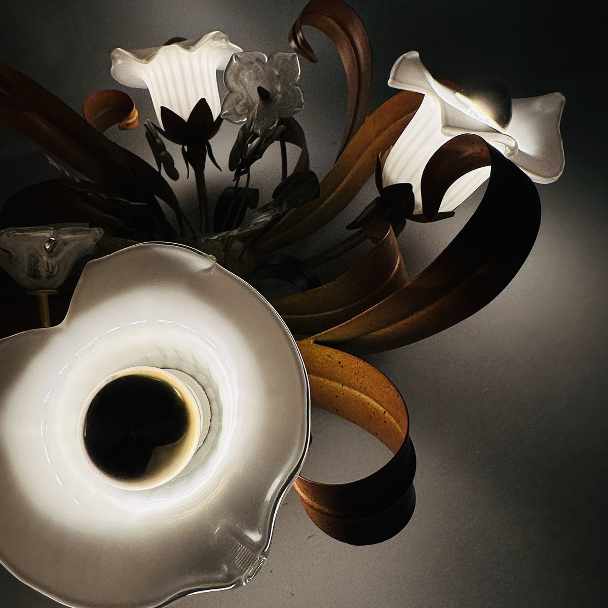 Eingeschaltete Calla-Glasschirme im Detail, warmes Licht und Schatten der Blattbänder an der Decke