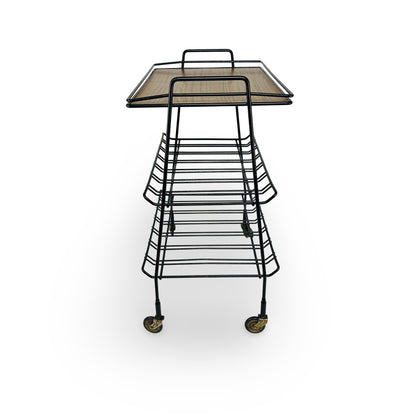 Short side of the serving trolley with handle, splayed legs and V-shaped bent racks
